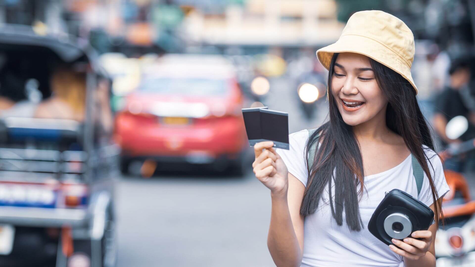 traveller-woman-holding-instant-camera-and-film-at-khao-san-road-bangkok-city-of-thailand-using-china-alipay-payment-tng-malaysia-red-car