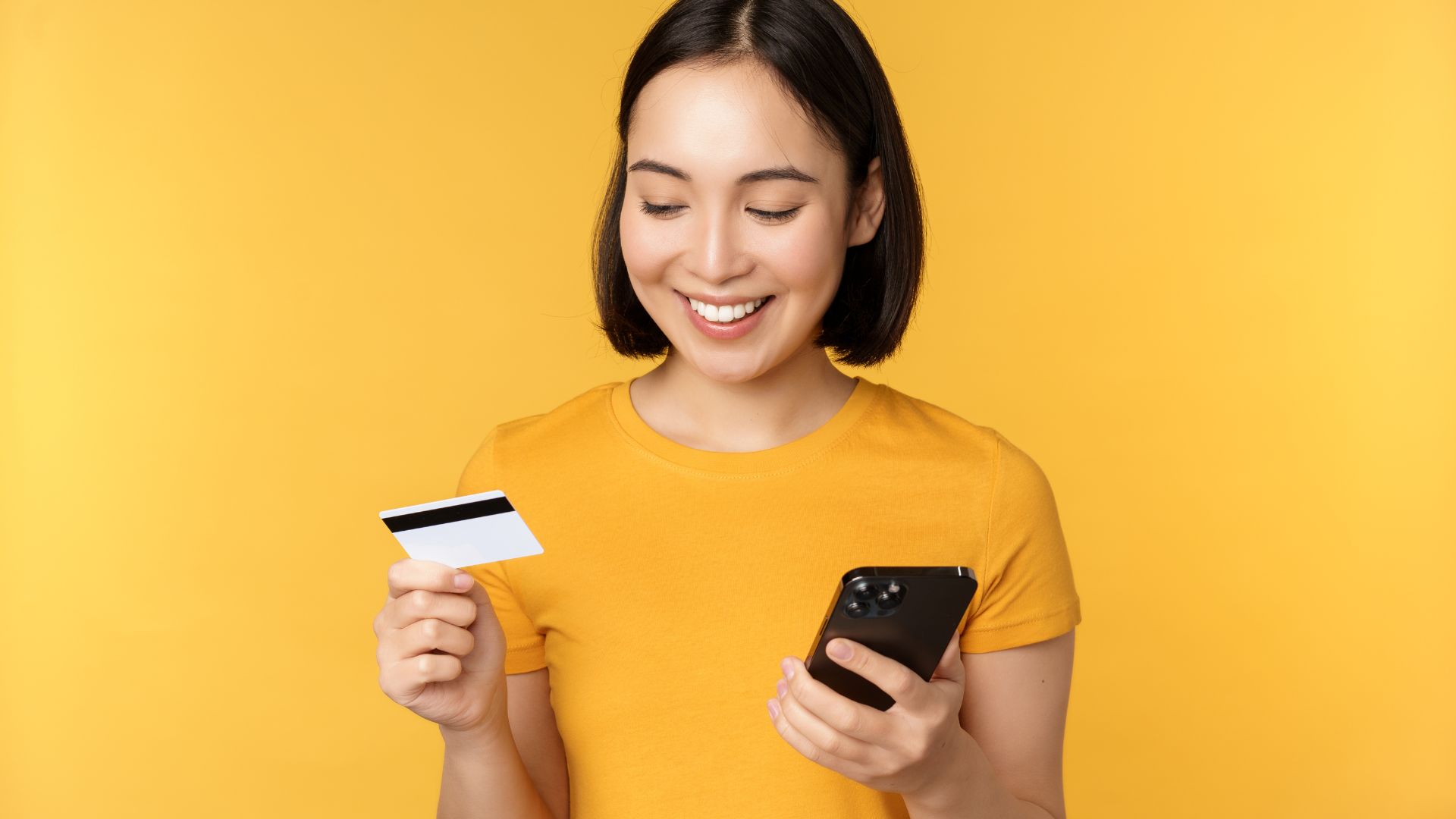 A girl in yellow shirt holding card and phone smiling happily for instalment application
