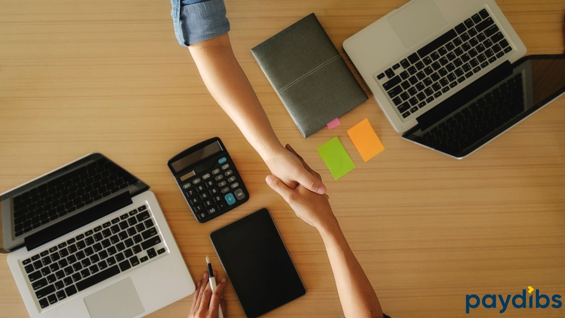 two person shaking hand with laptops and calculators on table