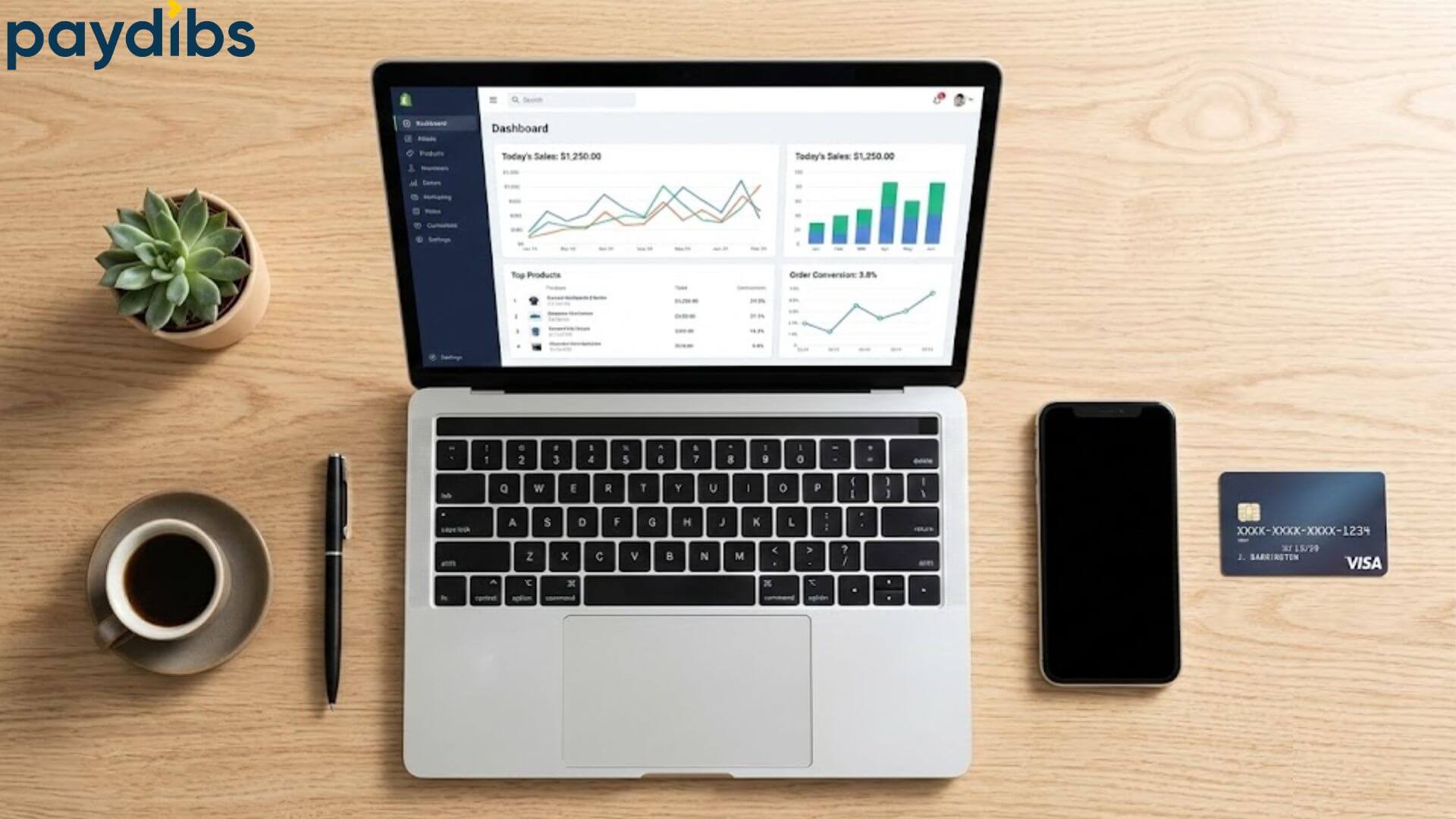 Top down plan view of a laptop on ecommerce dashboard screen on desk surrounded by mobile phone, coffee and card