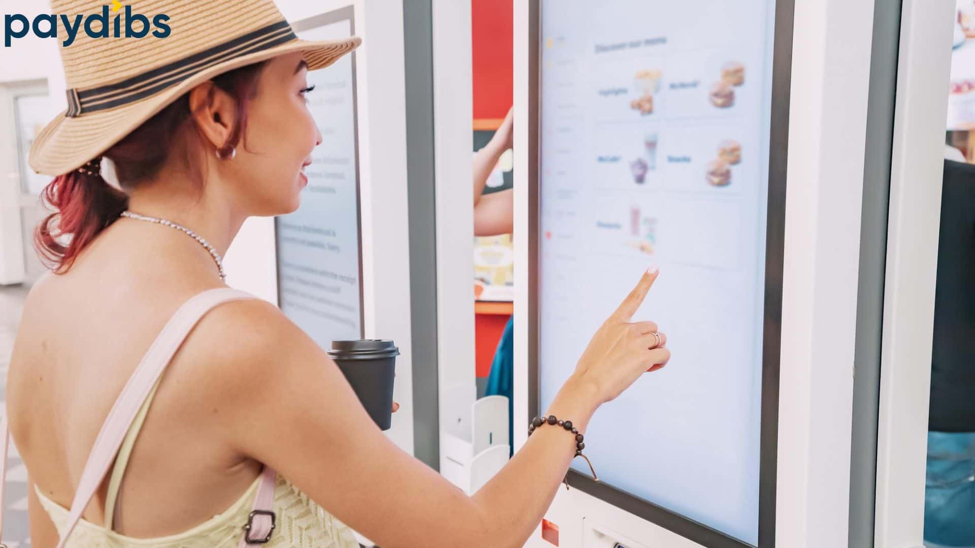A female customer using self service kiosk machine terminal to order food at restaurant